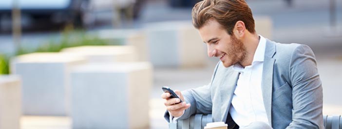 Happy businessman looking at mobile phone seated on park bench